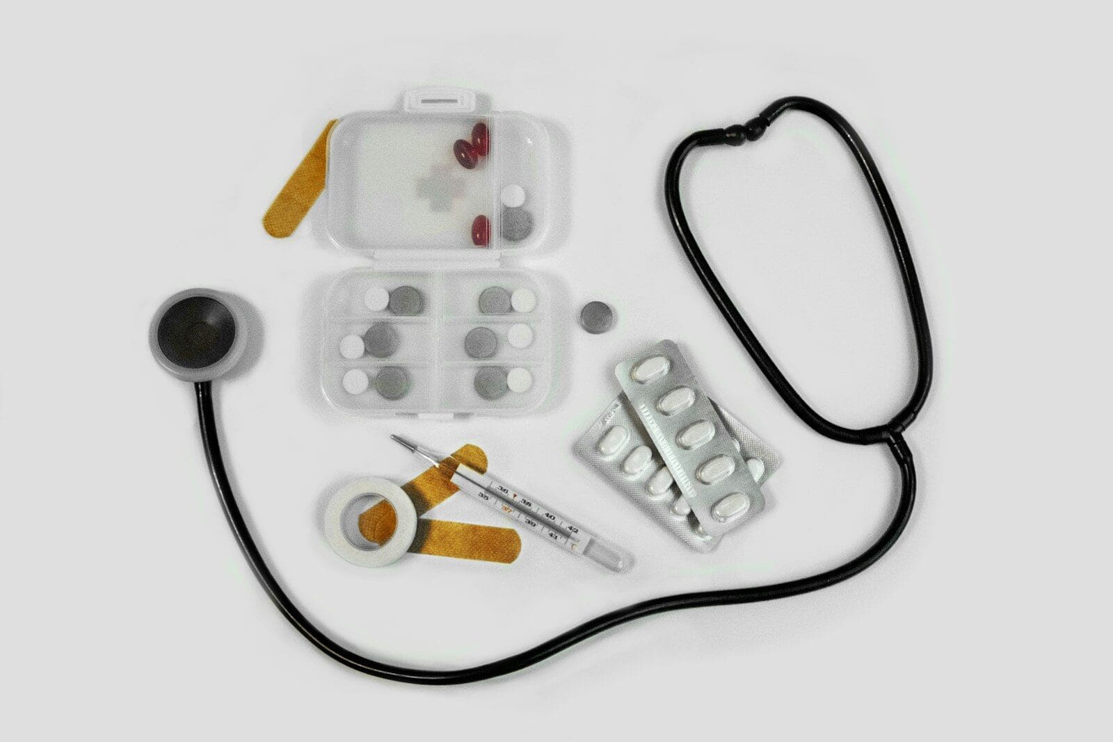 A stethoscope, pill organizer, blister packs, thermometer, and adhesive bandages on white